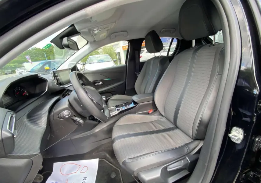 Vue intérieure côté conducteur de la Peugeot 208 noire 2021 avec sièges gris clair et tableau de bord moderne.