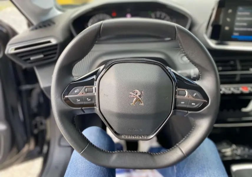 Vue centrée sur le volant cuir noir de la Peugeot 208 2021 avec commandes intégrées et tableau de bord en arrière-plan.