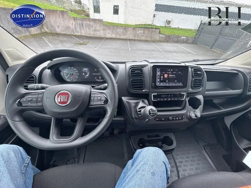 Vue intérieure frontale du tableau de bord du Fiat Ducato Benne blanc 2023 avec volant multifonction et écran tactile central.