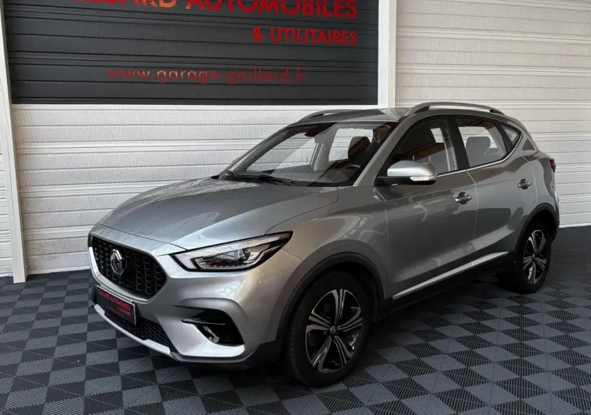 MG ZS gris clair vu en 3/4 avant droit dans un showroom avec jantes noires et toit ouvrant.