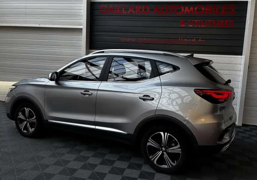 Vue de profil côté gauche d'un MG ZS gris clair 2022 avec jantes alliage et barres de toit chromées.