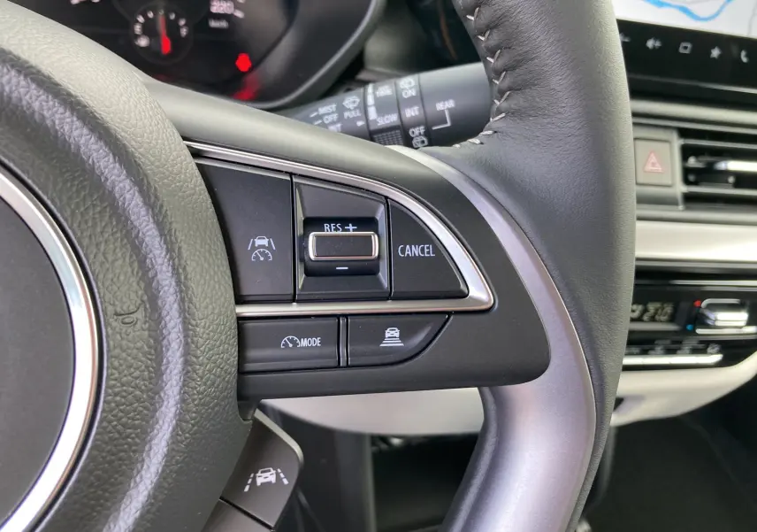 Gros plan sur le volant cuir multifonctions de la Suzuki Swift 2025, boutons de régulateur de vitesse et assistance active visibles.