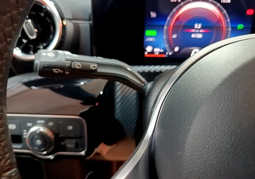 Gros plan intérieur sur le volant et le combiné d'instruments numérique bleu de la Mercedes Classe A noire.