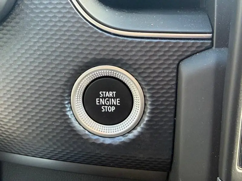 Gros plan sur le bouton Start Engine Stop entouré d'un cerclage argenté, sur la console intérieure texturée du Renault Arkana gris métallisé.