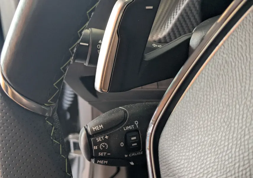 Gros plan sur la commande de régulateur de vitesse au volant noir avec surpiqûres vertes du Peugeot 208 Hybrid 145 e-DCS6 GT.