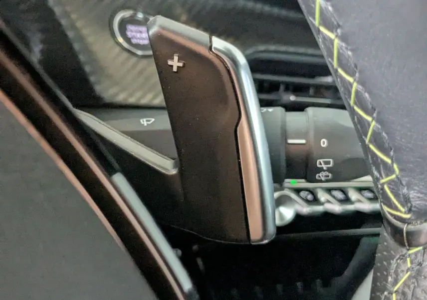 Gros plan sur la palette de changement de vitesse "+" côté droit du volant avec surpiqûres vertes dans un Peugeot 208 gris Selenium.