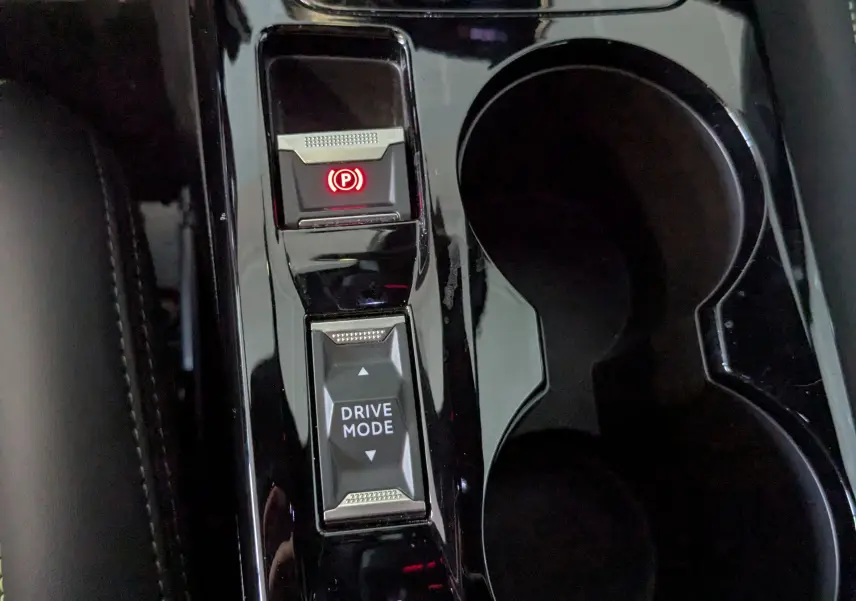 Gros plan sur la console centrale noire brillante de la Peugeot 208 Hybrid 145 e-DCS6 GT avec bouton frein à main électronique et mode de conduite.