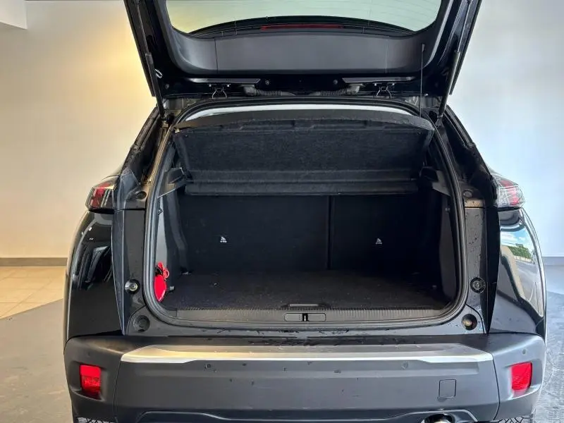 Coffre ouvert vu de l'arrière d'un Peugeot 2008 noir Perla Nera avec hayon relevé et feux arrière LED visibles.