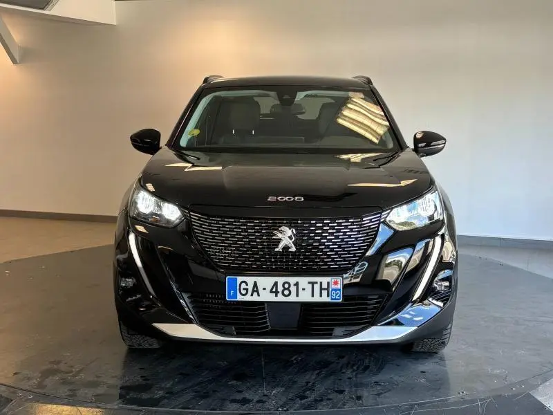 Vue frontale d'un Peugeot 2008 noir Perla Nera avec calandre distinctive et phares LED allumés dans un intérieur sobre.