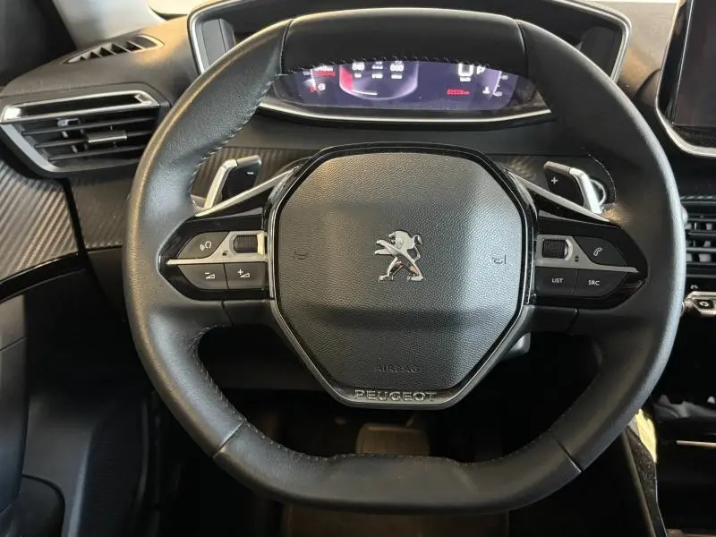 Vue rapprochée du volant cuir noir multifonction du Peugeot 2008 2021 avec tableau de bord numérique en arrière-plan.