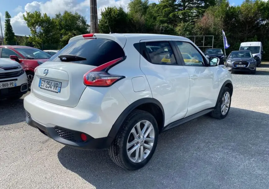 Nissan Juke blanc métallisé vu en 3/4 arrière droit, avec jantes alliage 17 pouces sport et vitres arrière surteintées.