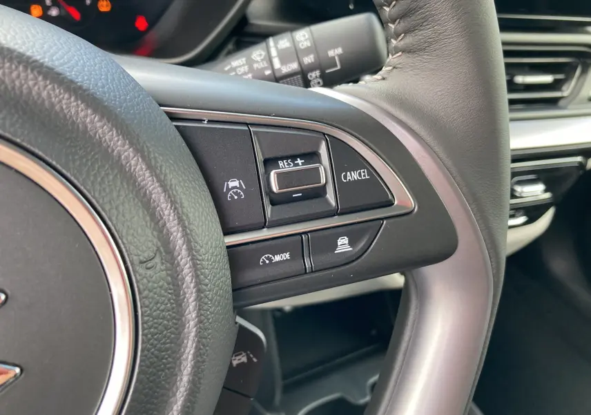 Gros plan sur les commandes du volant cuir noir de la Suzuki Swift 2025, avec régulateur de vitesse et aides à la conduite.