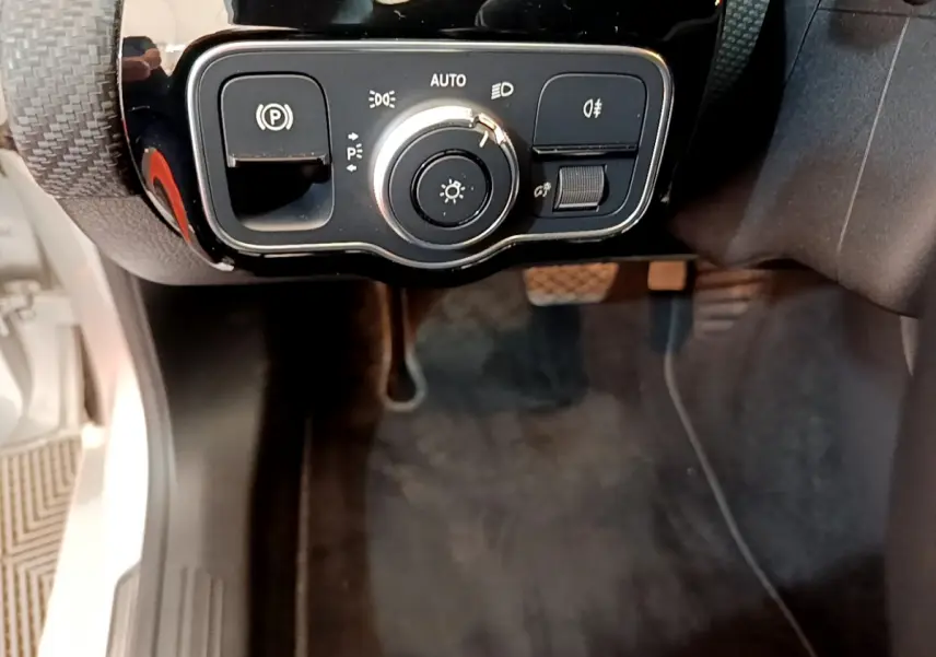 Gros plan sur la commande des phares et frein à main électrique côté gauche d’une Mercedes Classe A gris clair.