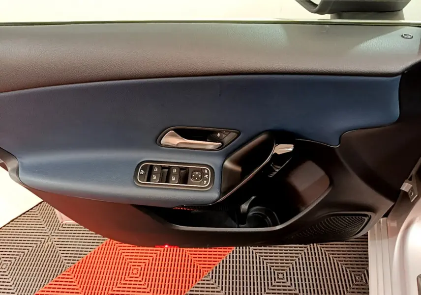 Vue intérieure du panneau de porte côté conducteur d'une Mercedes Classe A 180 d Business Line gris clair, avec commandes de vitres et poignée chrome.