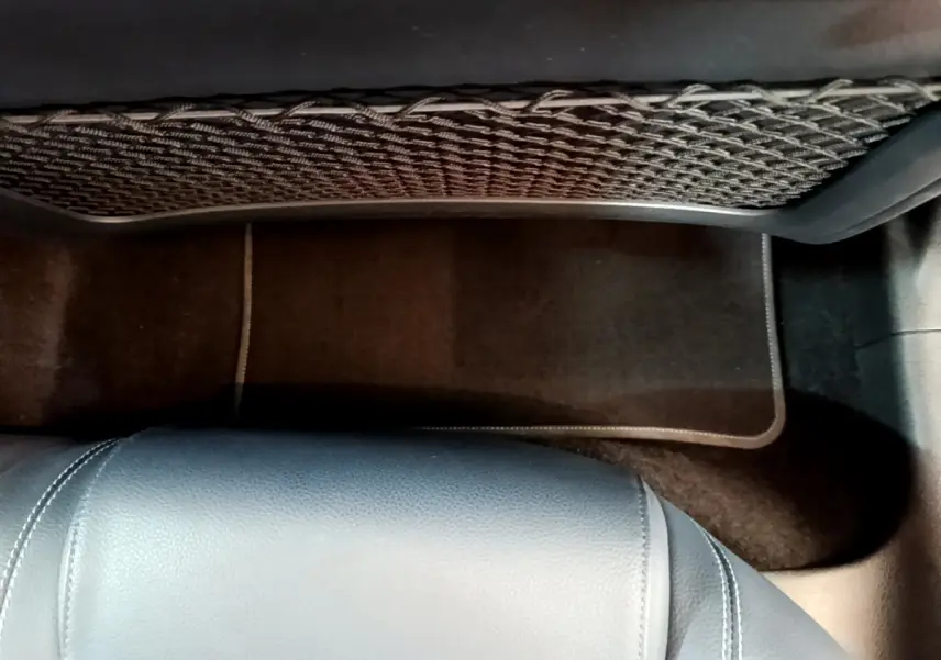 Vue intérieure du plancher arrière avec tapis noir et filet de rangement sur le dossier du siège avant d'une Mercedes Classe A gris clair.