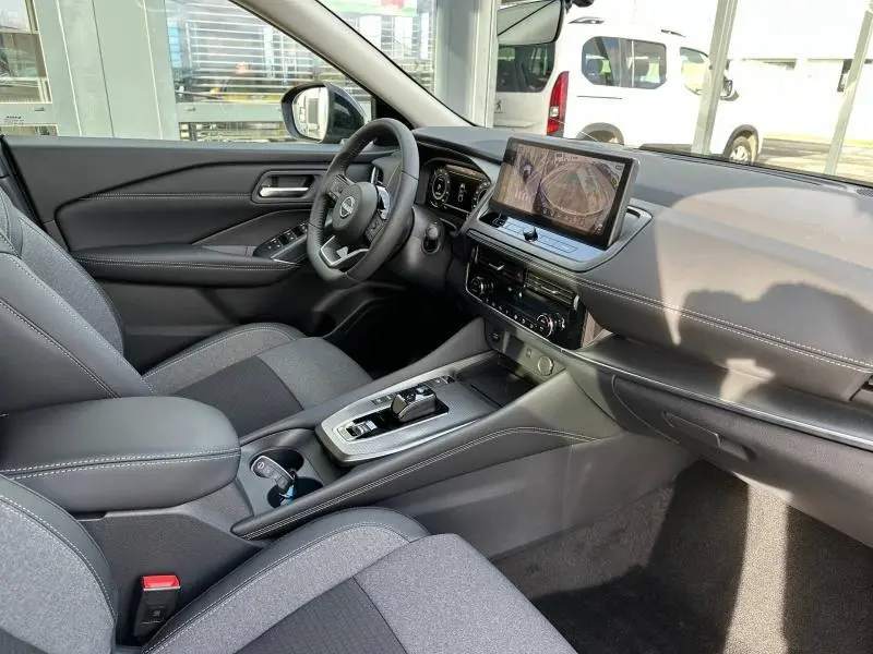 Vue intérieure côté conducteur du Nissan Qashqai Hybrid e-POWER 2025, tableau de bord moderne avec écran tactile et sellerie grise.