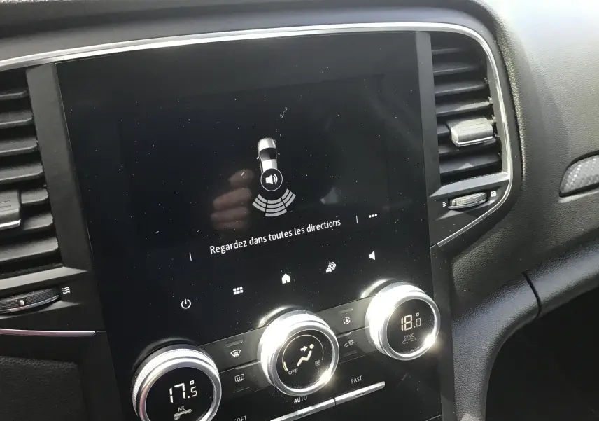 Vue rapprochée de la console centrale noire de la Renault Mégane IV Société blanche, avec écran tactile et commandes de climatisation.