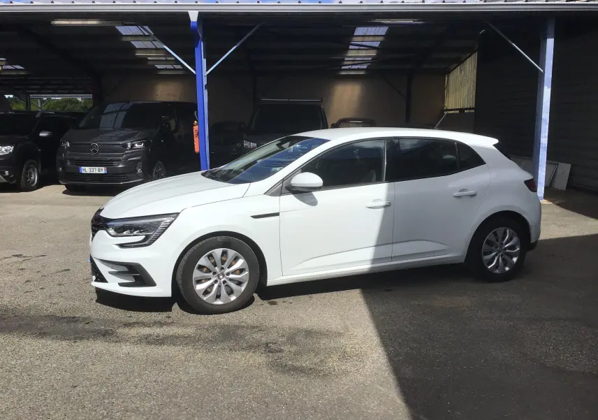 Renault Mégane IV Société blanche vue de profil côté gauche, stationnée à l'extérieur sous un abri partiel.