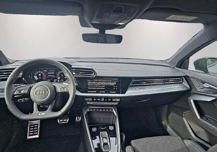Vue intérieure avant de l'Audi A3 Sportback gris Daytona 2026, volant sport multifonction et écran tactile central.