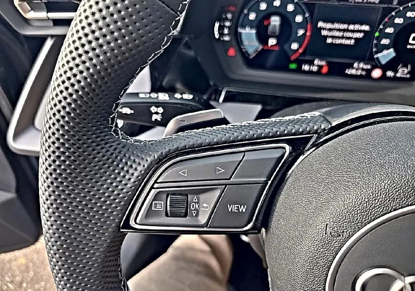 Gros plan sur le volant cuir perforé et les commandes multifonctions à gauche de l'Audi A3 Sportback gris Daytona 2026.