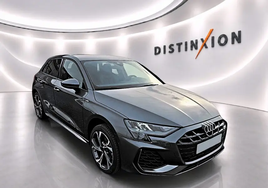Audi A3 Sportback gris Daytona vue 3/4 avant droit dans un showroom lumineux avec logo Distinxion en arrière-plan.
