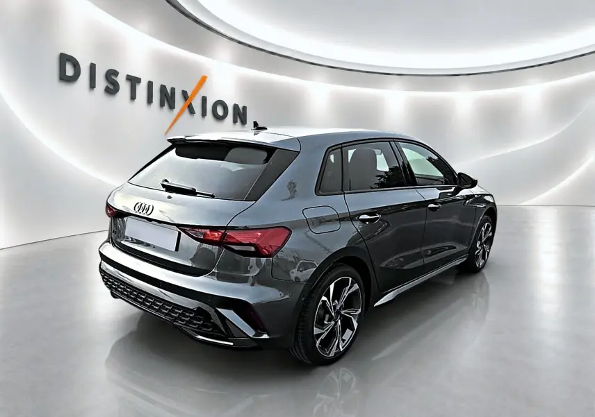 Audi A3 Sportback gris Daytona vue 3/4 arrière droit dans un showroom lumineux avec jantes alu distinctives.