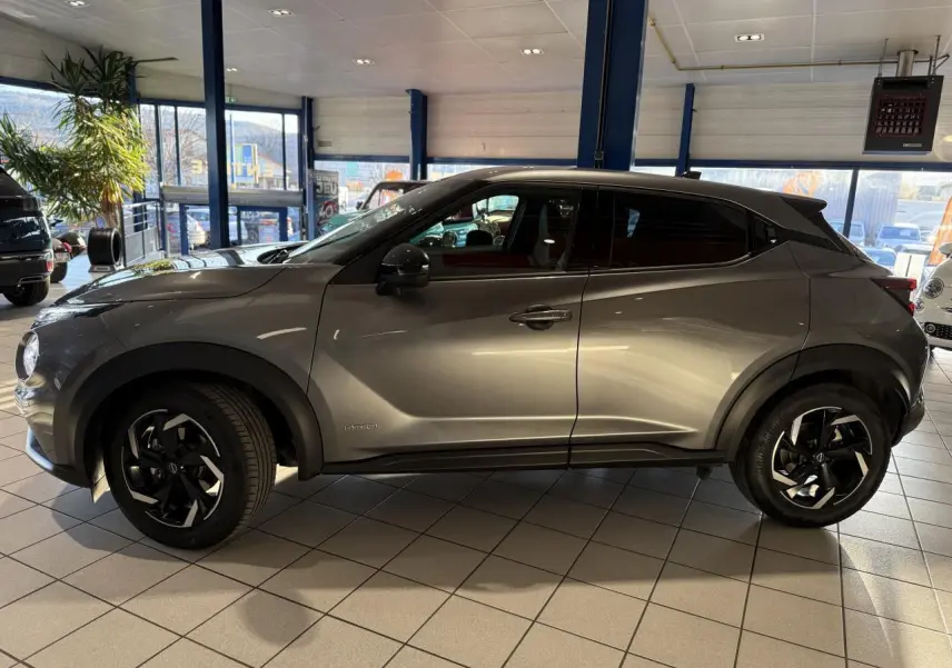 Profil côté gauche du Nissan Juke Hybrid 143 N-Connecta gris métallisé en showroom avec jantes alliage noires.