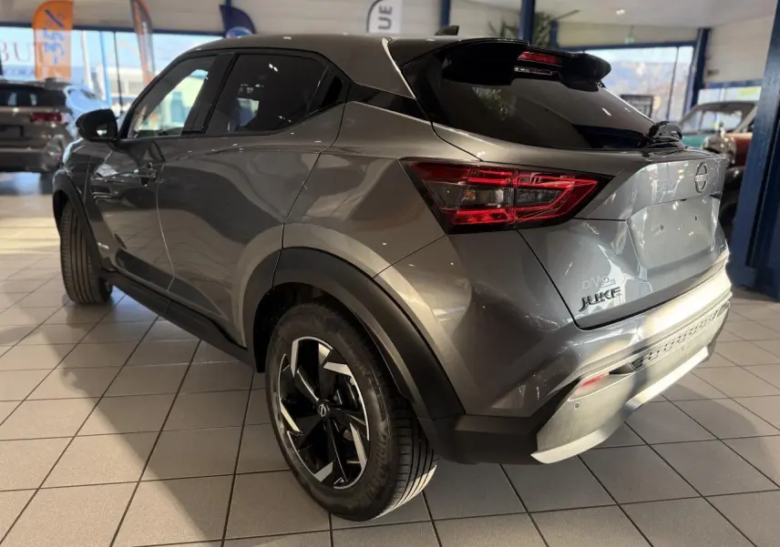Vue 3/4 arrière droite du Nissan Juke Hybrid gris métallisé avec jantes alliage et toit noir en showroom.