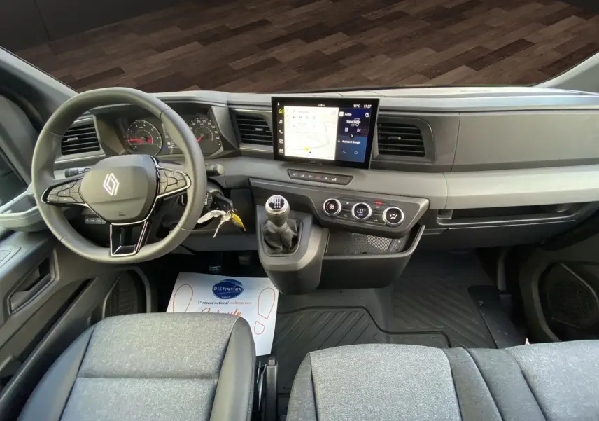 Vue intérieure frontale du tableau de bord du Renault Master 2025 avec volant, écran tactile et banquette passager grise.