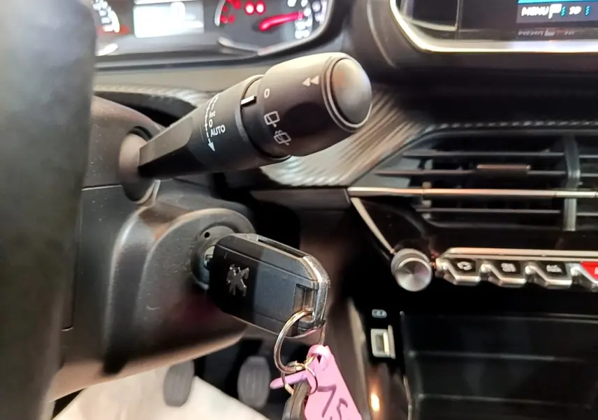 Gros plan sur le contacteur avec clé Peugeot insérée, volant cuir et tableau de bord noir du Peugeot 2008 blanc.