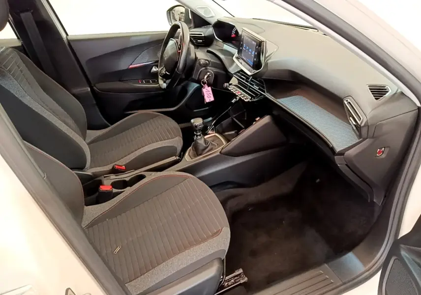 Vue intérieure côté conducteur du Peugeot 2008 blanc, montrant le tableau de bord et la console centrale avec écran tactile.