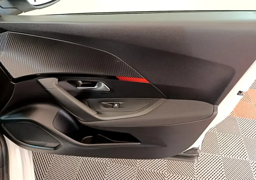 Vue intérieure de la porte côté conducteur d’un Peugeot 2008 blanc, avec insert noir texturé et bande rouge.