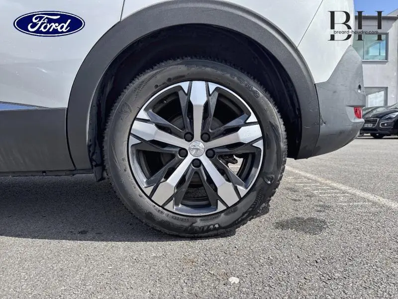 Gros plan sur la roue arrière droite d’un Peugeot 5008 blanc nacré avec jante alliage et logo Peugeot au centre.