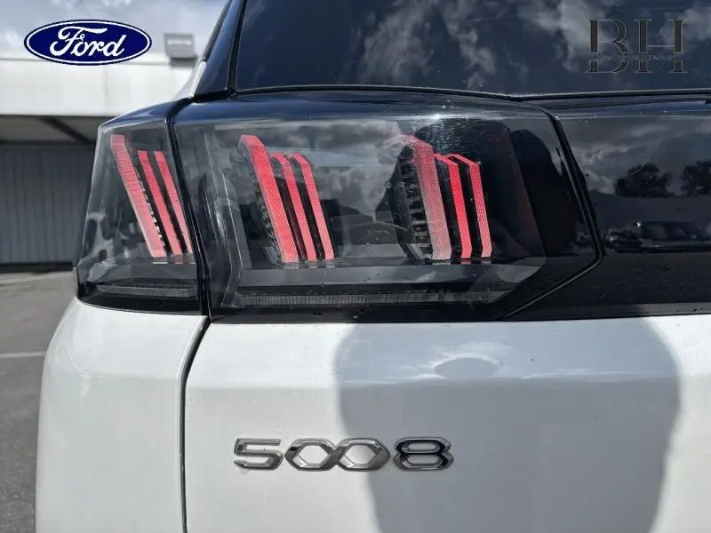 Gros plan sur le feu arrière droit et le logo 5008 d’un Peugeot 5008 blanc nacré, arrière du véhicule visible.
