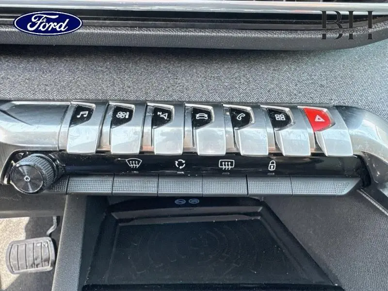 Gros plan sur la rangée de boutons argentés et noirs du tableau de bord d’un Peugeot 5008 blanc nacré, avec bouton rouge d’alerte.