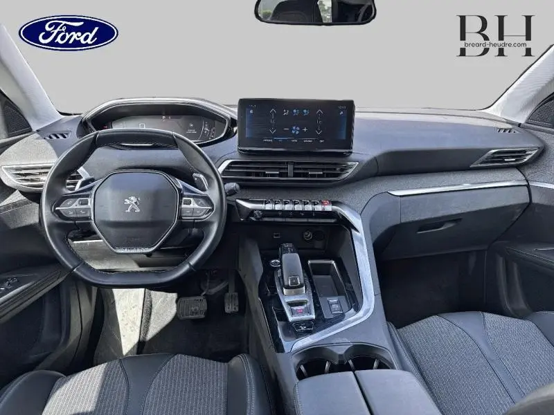 Vue intérieure avant du Peugeot 5008 avec tableau de bord moderne, volant compact et écran tactile central.