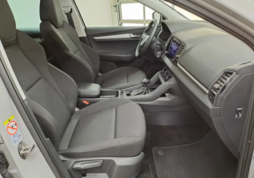 Vue intérieure côté conducteur du Skoda Karoq 2023 gris perle, mettant en valeur les sièges noirs et le tableau de bord moderne.