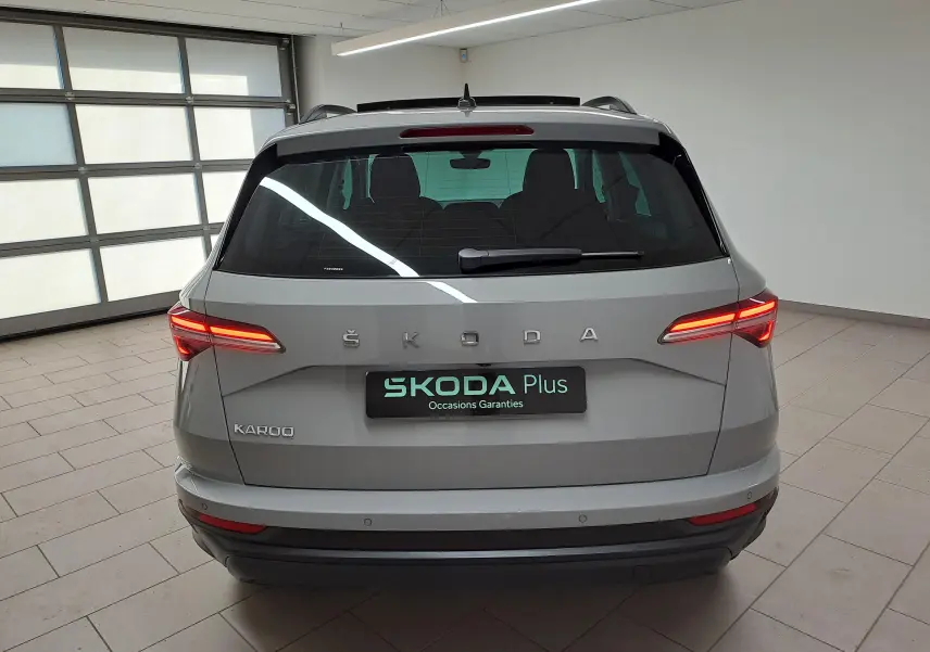 Vue arrière d'un Skoda Karoq gris perle 2023 avec feux allumés dans un garage lumineux.