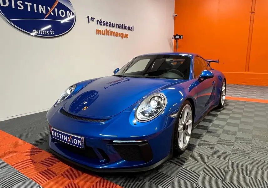 Porsche 911 GT3 bleu saphir vue 3/4 avant droit, avec aileron arrière et jantes argentées en showroom.
