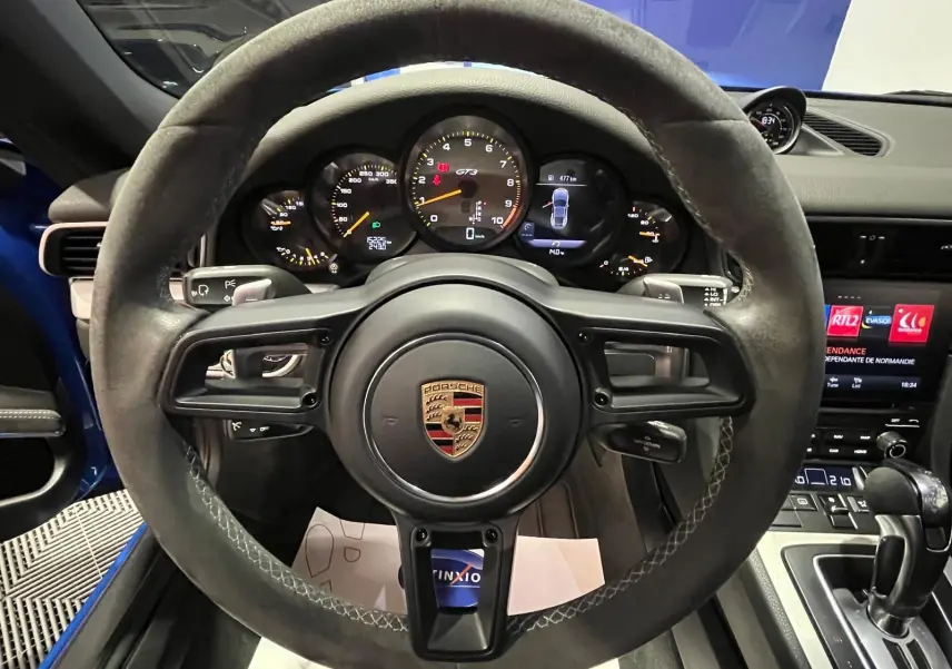 Vue intérieure centrée sur le volant sport alcantara et le tableau de bord de la Porsche 911 GT3 bleu saphir.