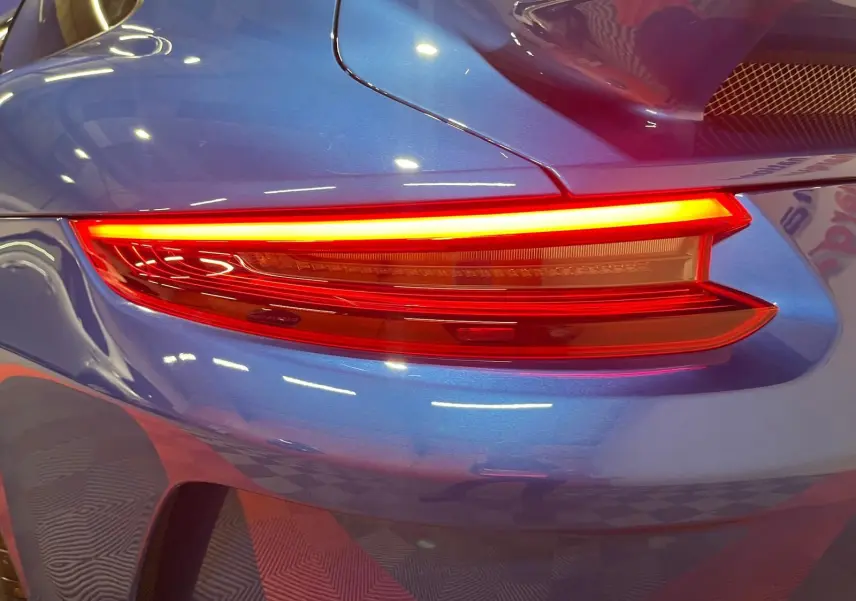 Gros plan sur le feu arrière droit d'une Porsche 911 GT3 bleu saphir, soulignant la finition sportive et les courbes élégantes.