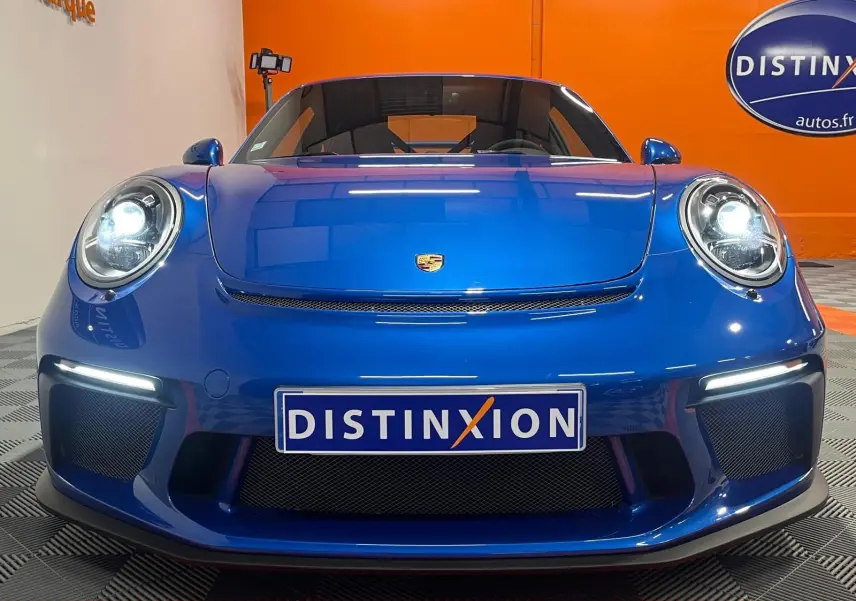 Vue frontale rapprochée de la Porsche 911 GT3 bleu saphir avec phares allumés et plaque Distinxion.