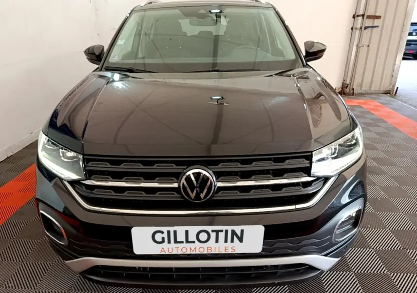 Vue avant d’un Volkswagen T-Cross noir 2022 avec calandre chromée et phares LED allumés dans un garage.