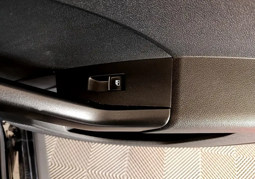 Gros plan sur la commande de verrouillage de porte côté conducteur d’un Volkswagen T-Cross noir, intérieur sombre.