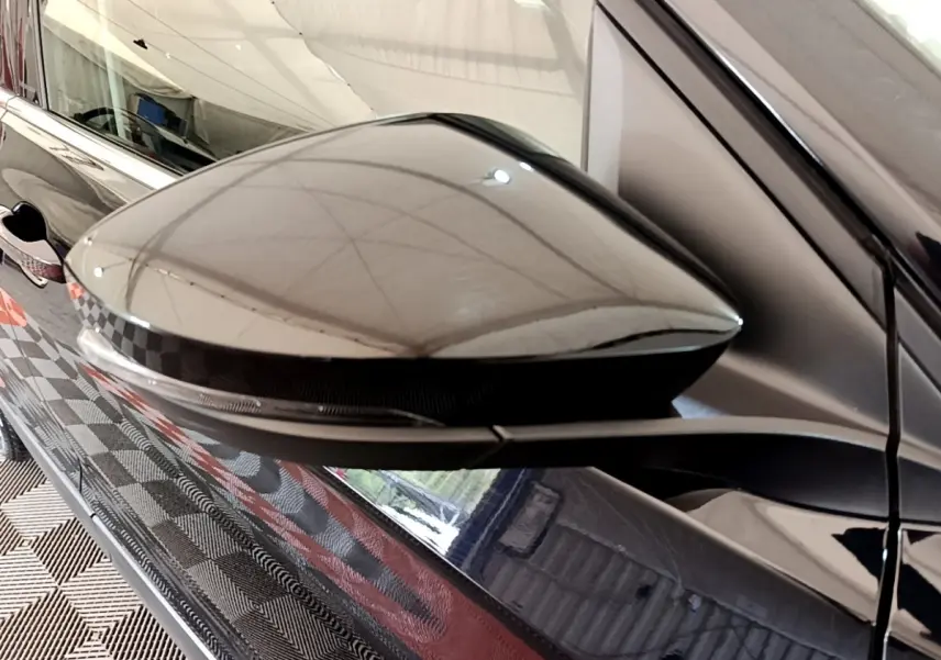 Gros plan sur le rétroviseur droit noir brillant du Volkswagen T-Cross 2022 avec reflet de l'environnement intérieur.