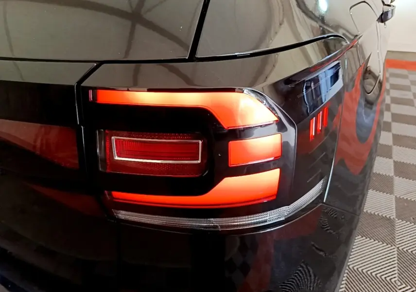 Gros plan sur le feu arrière droit rouge allumé d’un Volkswagen T-Cross noir, avec reflet sur la carrosserie brillante.