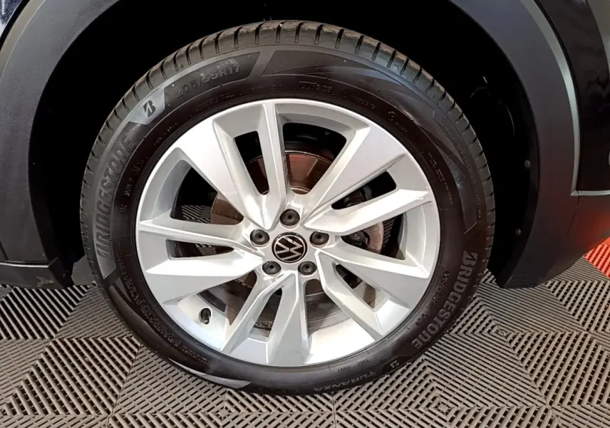 Gros plan sur la roue avant droite du Volkswagen T-Cross noir, jante alliage argentée avec logo VW central.