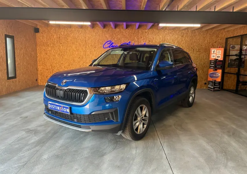 SUV SKODA KODIAQ bleu 2023 en 3/4 avant droit, avec calandre noire et jantes argentées, dans un showroom intérieur.