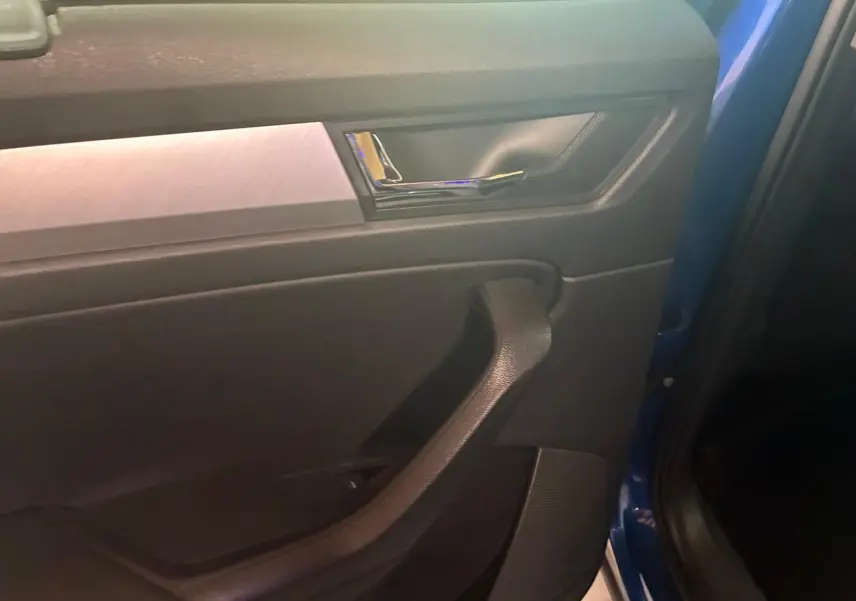 Vue intérieure du panneau de porte côté gauche d'un Skoda Kodiaq bleu 2023 avec poignée noire et insert décoratif gris.