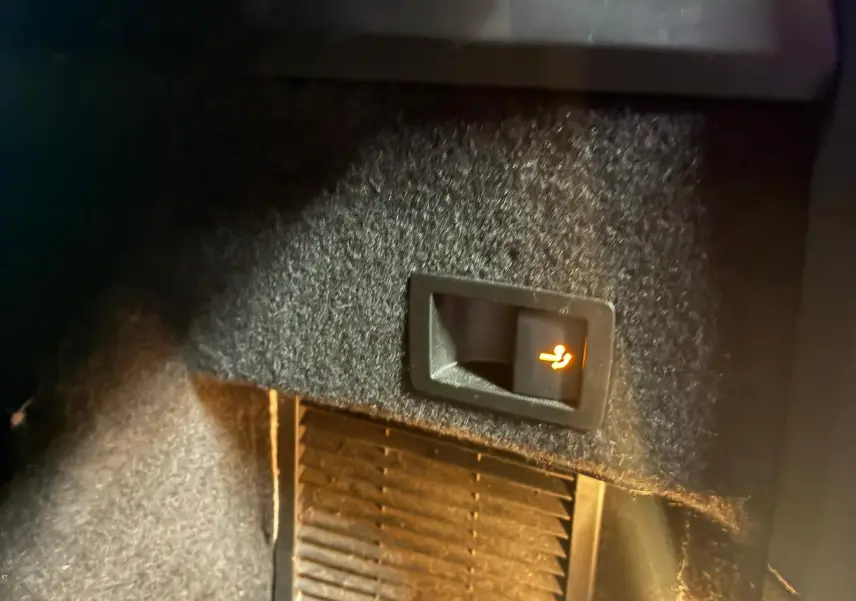 Détail intérieur montrant un bouton de déverrouillage de siège arrière illuminé sur un Skoda Kodiaq bleu 2023.